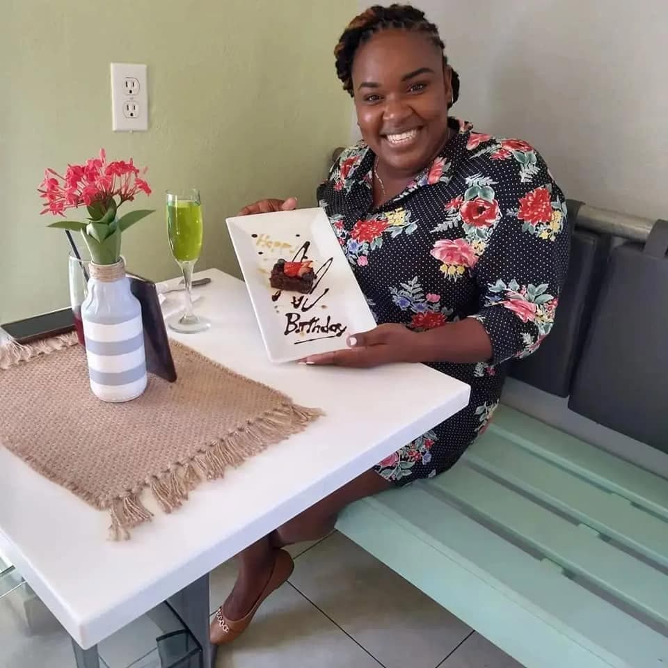 A guest holding up her birthday dessert plate at an indoor table, a green cocktail beside her