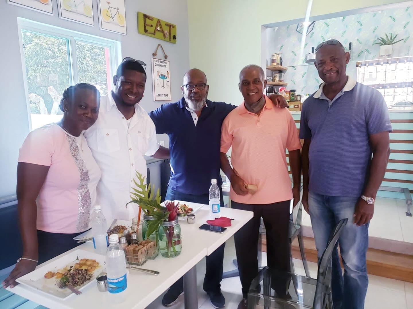 Five friends with arms around each other gathered around a table of shared plates