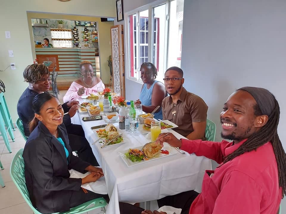 A group of six friends sharing sandwiches and salads around a long table indoors