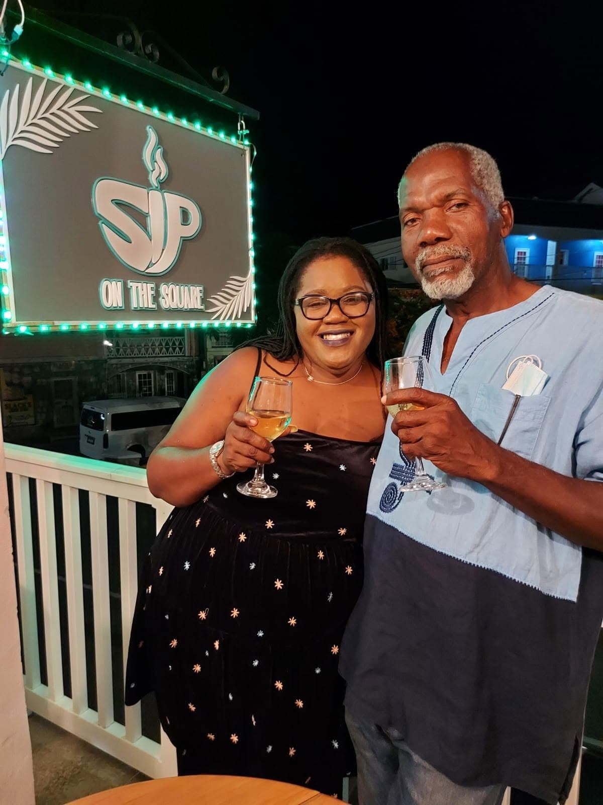 Two guests toasting with wine glasses beneath the illuminated SIP ON THE SQUARE sign at night