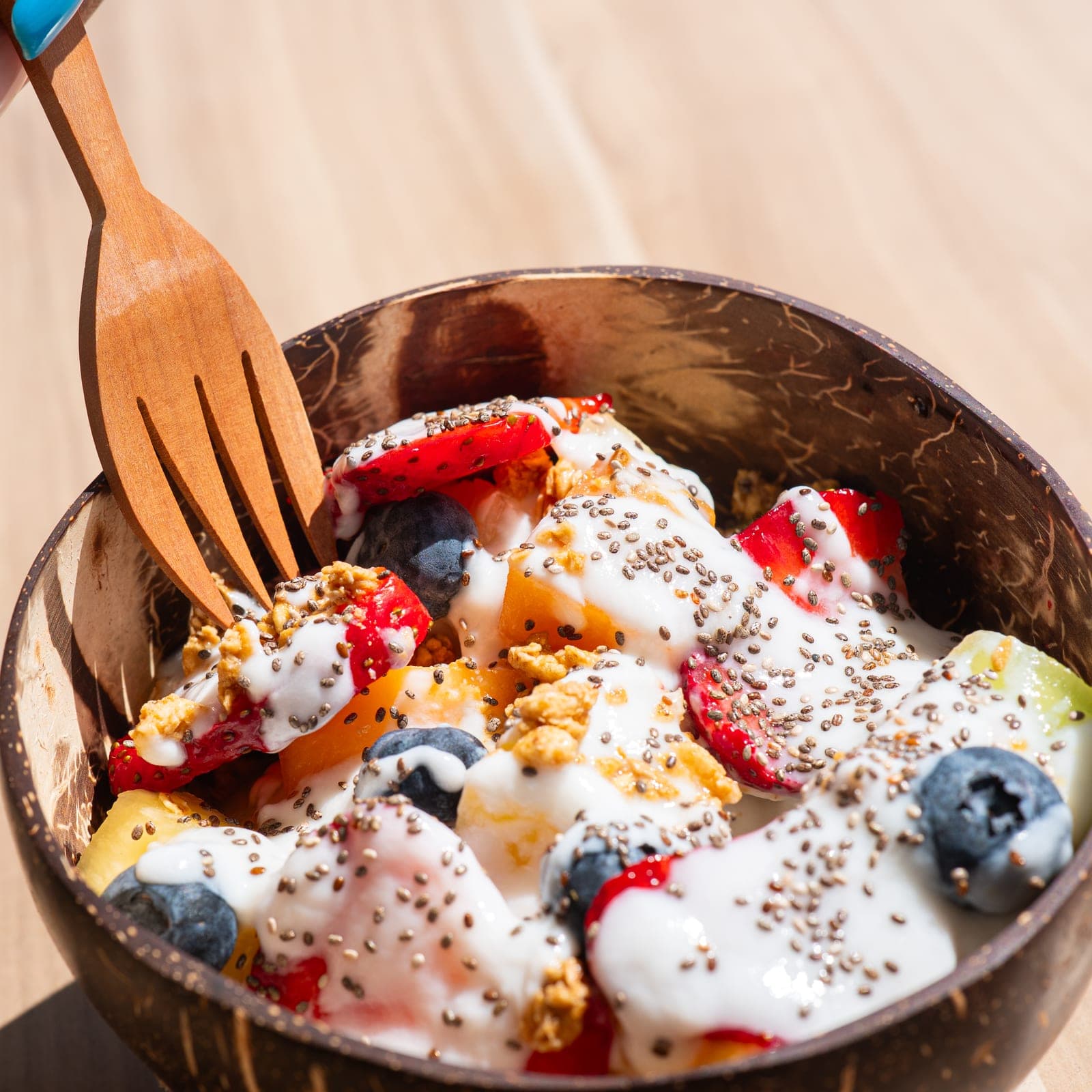 A yoghurt and fruit parfait in a coconut bowl, held up on the veranda