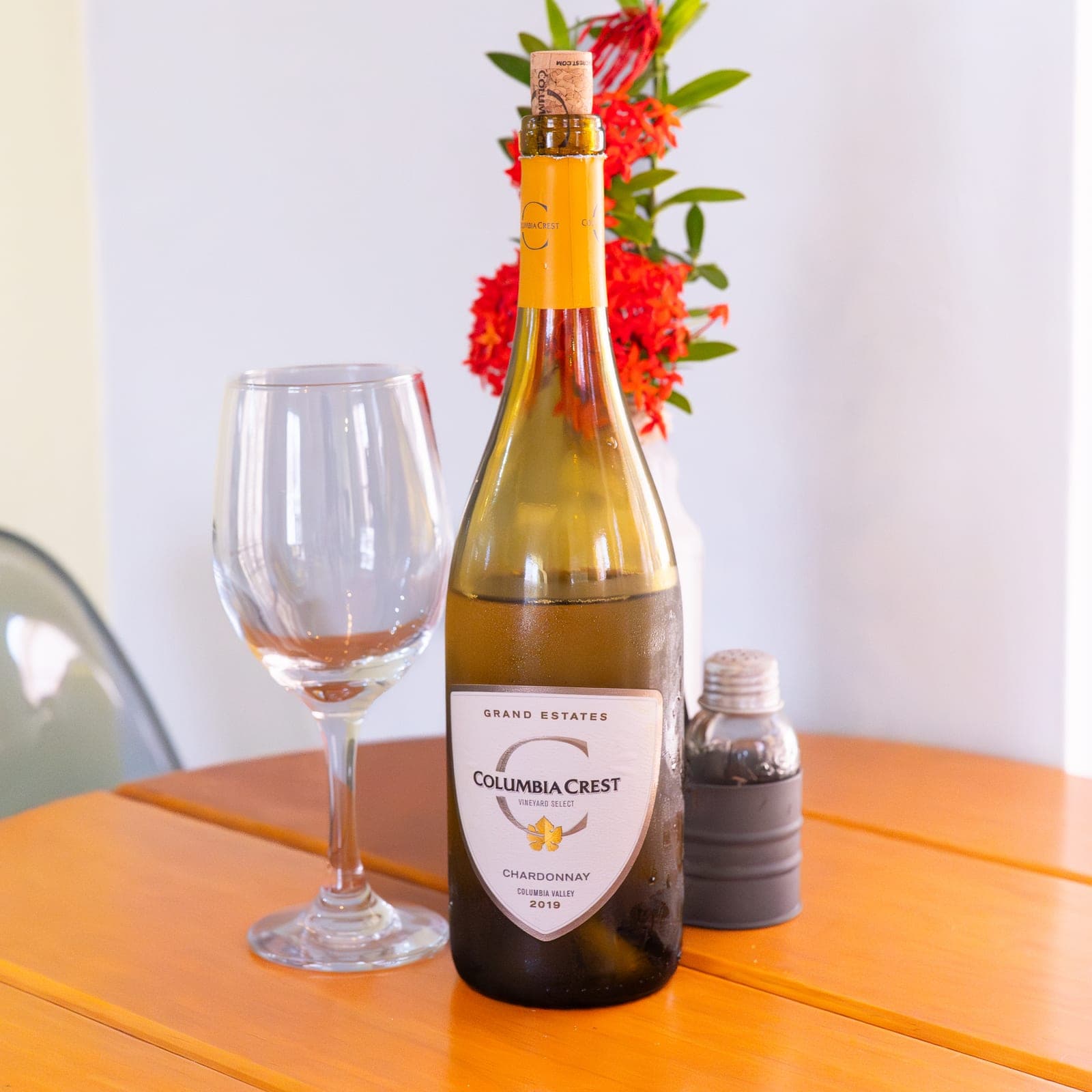 A bottle of white wine and a glass set on the veranda table, ixora flowers behind