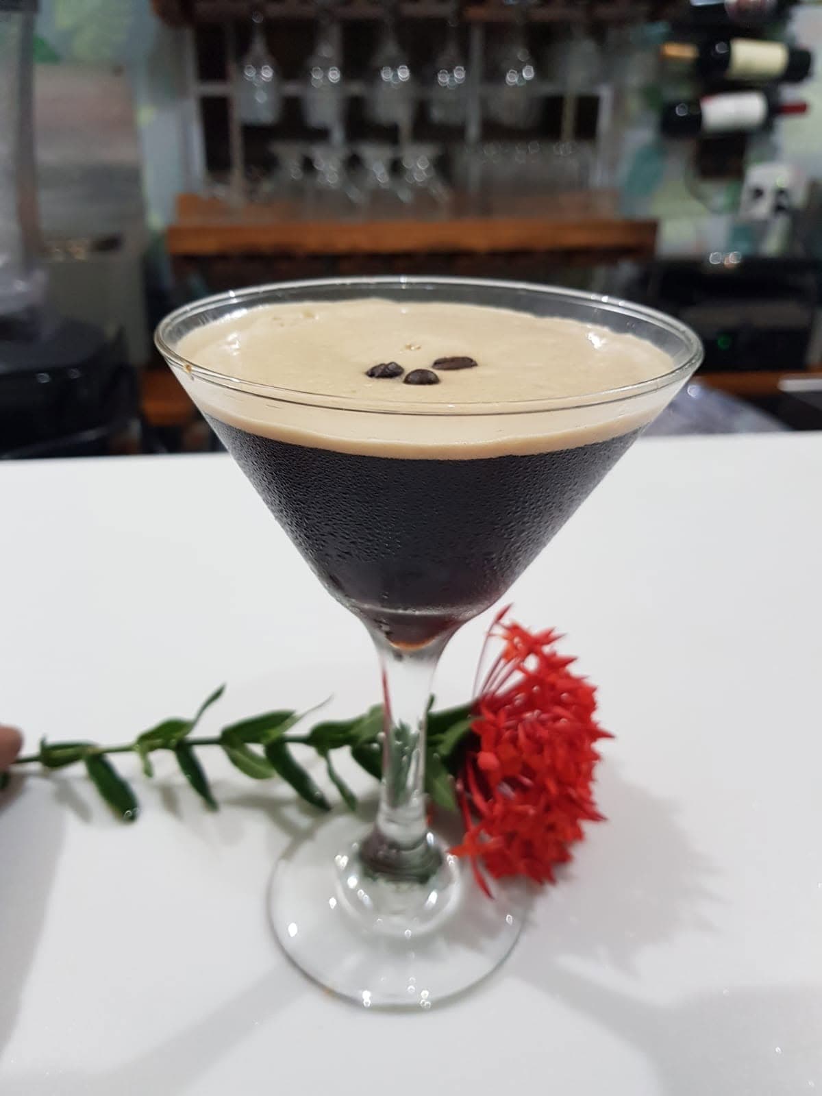 An espresso martini garnished with a red ixora flower, served at the bar